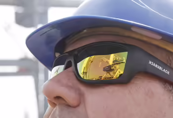 In der Nahansicht der Sonnenbrille im Gesicht eines NEUERO Mitarbeiters spiegelt sich ein Verladeturm.