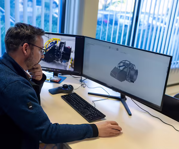 Ein NEUERO Mitarbeiter arbeitet konzentriert am Schreibtisch, auf dem Bildschirm vor ihm ein 3D-Modell eines Maschinenteils. 